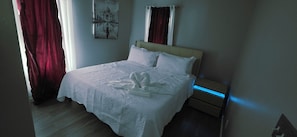 Une chambre d’hôtel avec un lit, une table de chevet, une lampe fixée au mur et un tableau représentant le Taj Mahal.