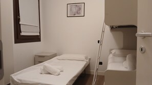 Ein Zimmer mit einem Einzelbett, einem Nachttisch, einer kleinen Kommode, einem gerahmten Bild an der Wand und einer Tür zu einem Badezimmer.
