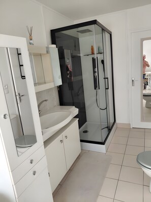 Un baño moderno con ducha de vidrio, lavamanos blanco y espejo.
