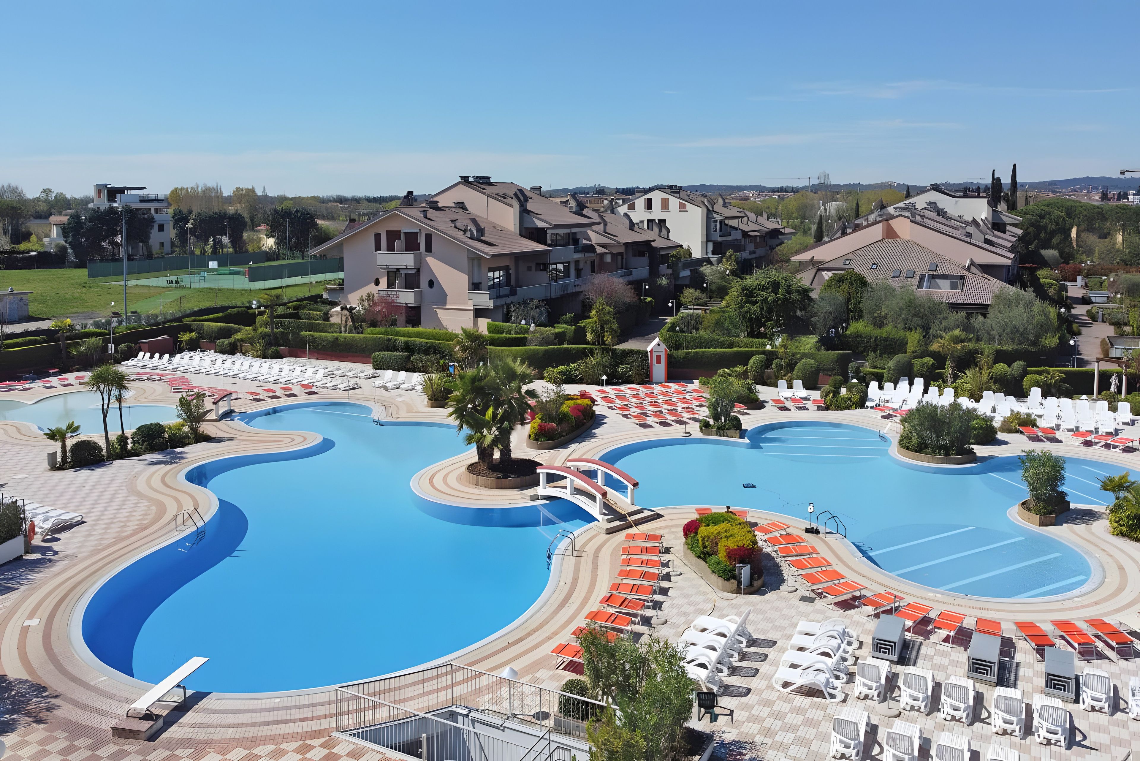 Un resort con una grande piscina, lettini prendisole e vista sui palazzi residenziali.