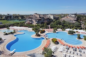 Un resort con una grande piscina, lettini prendisole e vista sui palazzi residenziali.