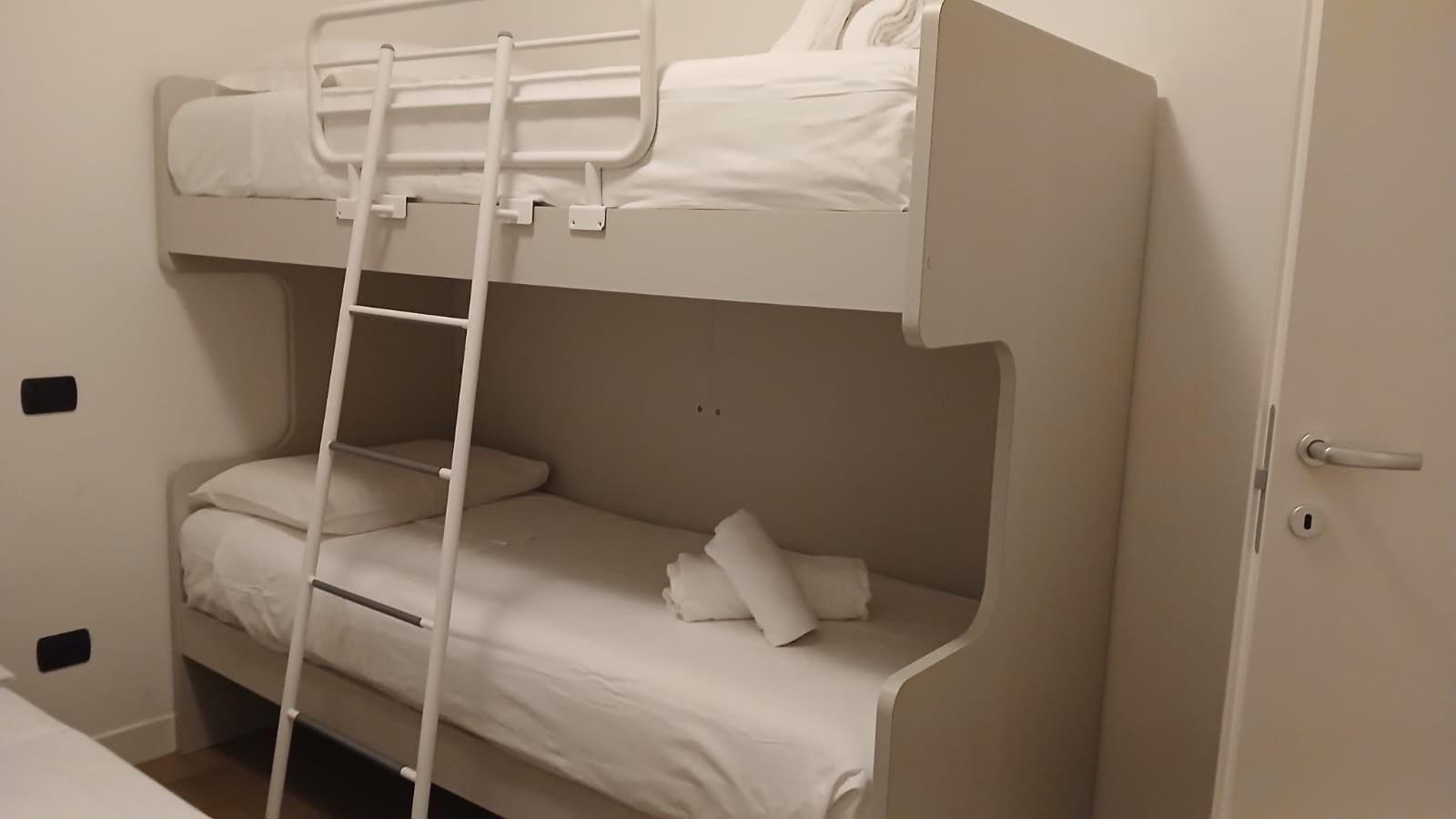 Un letto a castello con una scala, biancheria bianca e una porta con maniglia.