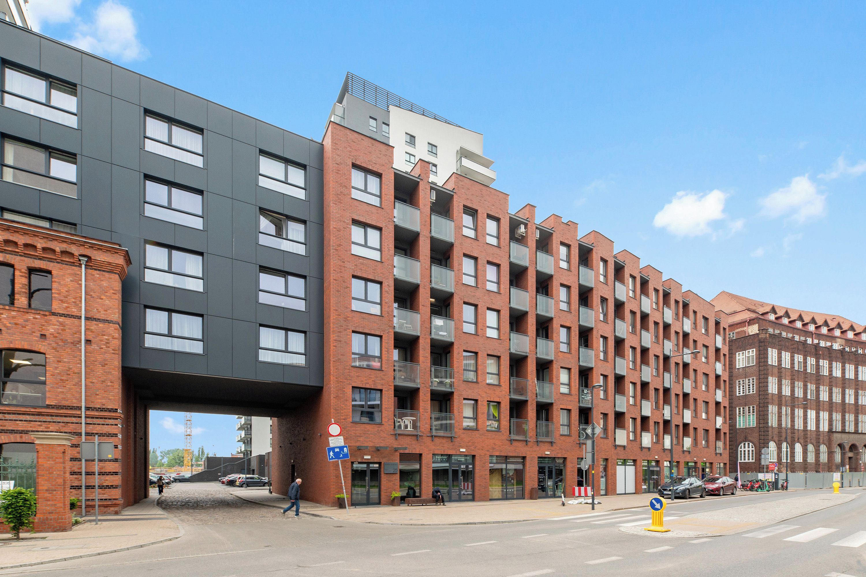 A multi-story building with a modern architectural design, featuring a mix of brick and concrete facades, large windows, and a pedestrian overpass.