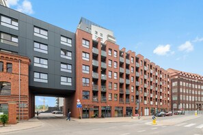A multi-story building with a modern architectural design, featuring a mix of brick and concrete facades, large windows, and a pedestrian overpass. - Hello Gdańsk Wałowa with Parking (Gdańsk)