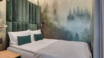 A bedroom with a bed, two pillows, a nightstand, and a wall mural of a forest scene.