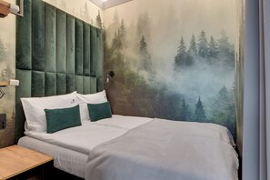 Ein Schlafzimmer mit einem Bett, zwei Kissen, einem Nachttisch und einer Wandmalerei von Waldszene.