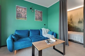 Ein Zimmer mit einer türkisfarbenen Wand, einem blauen Sofa, einem Holztisch und einem Bett mit Blick auf einen Wald.