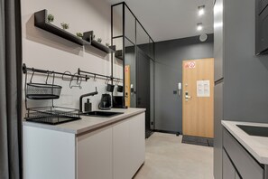 Eine moderne Küche mit Spüle, Wasserkocher und einem schwarzen Metallregal. Eine Holztür mit einem Schild und Lichtschalter ist ebenfalls zu sehen.