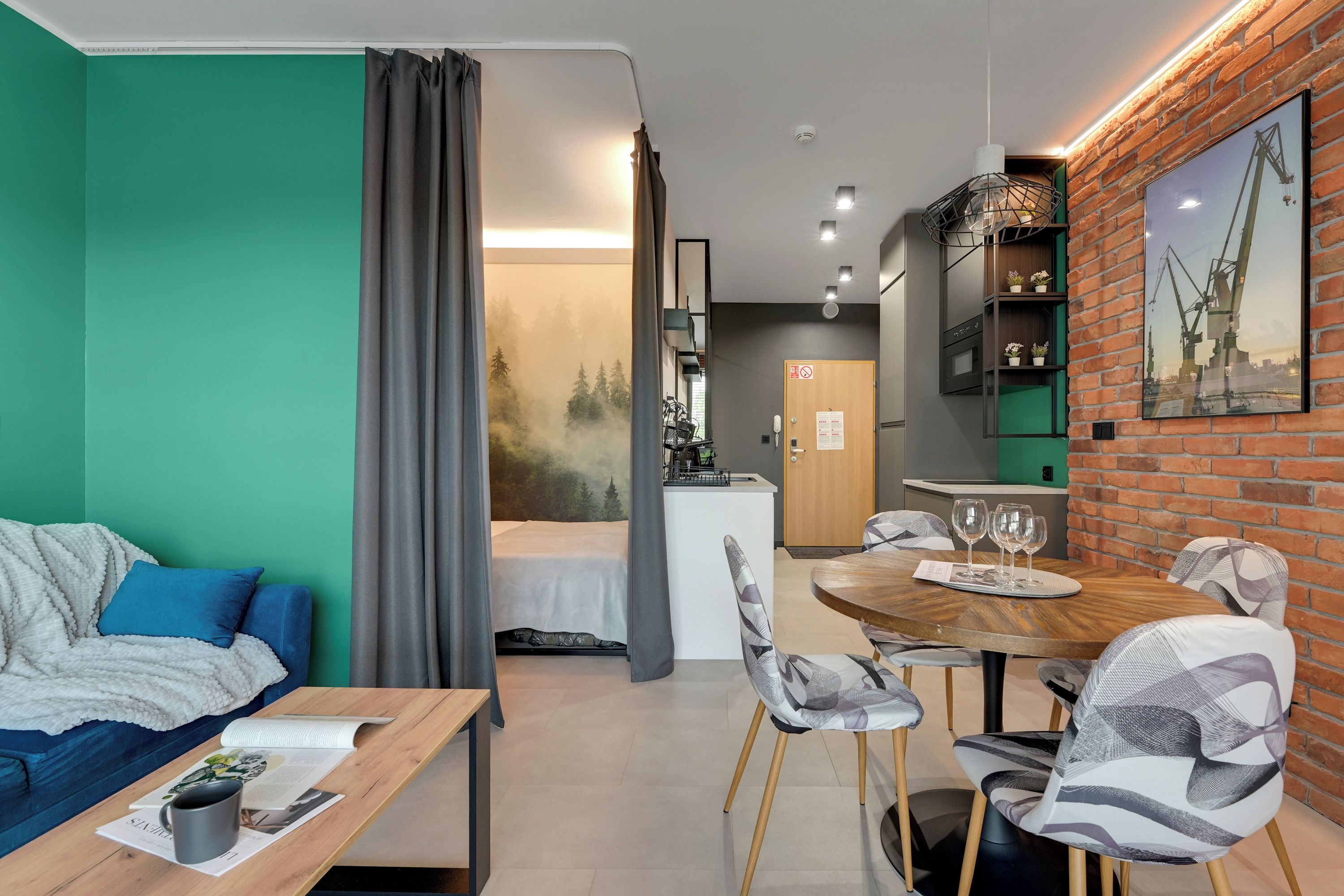 Een moderne hotelkamer met een bed, een eettafel met stoelen, een kitchenette en een zithoek met een bank en salontafel.