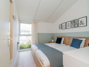 A bedroom with two beds, a window with curtains, and a wall with framed pictures. - Holiday Home in Renesse With Swimming Pool (Renesse)