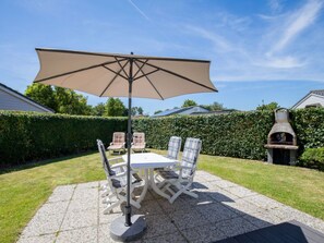 An outdoor patio with a table and chairs, a large umbrella, and a barbecue grill. - Holiday Home in Renesse With Swimming Pool (Renesse)