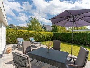 An outdoor patio with a table and chairs, a large umbrella, and a well-maintained hedge. - Holiday Home in Renesse With Swimming Pool (Renesse)