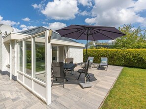 A covered patio area with a table and chairs, a large umbrella, and a view of the garden. - Holiday Home in Renesse With Swimming Pool (Renesse)