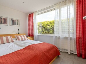 A bedroom with a bed, a nightstand, a window with curtains, and a view of greenery outside. - Holiday Home in Renesse With Swimming Pool (Renesse)