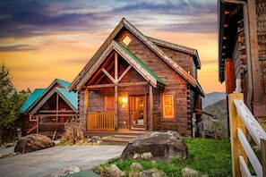 A log cabin with a prominent front porch, large windows, and a mountain backdrop. - Skyline Summit Long Range Views, Games, Hot Tub (Gatlinburg)