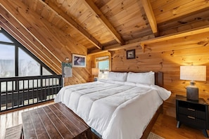 A wooden cabin bedroom with a bed, nightstand, and a view of the outdoors. - Skyline Summit Long Range Views, Games, Hot Tub (Gatlinburg)