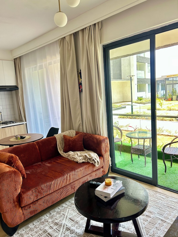 A modern living room with a sofa, a coffee table, and a view of an outdoor garden through a large window.