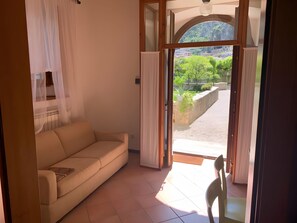 A room with a beige sofa, a wooden-framed window, and a view of greenery and buildings outside.