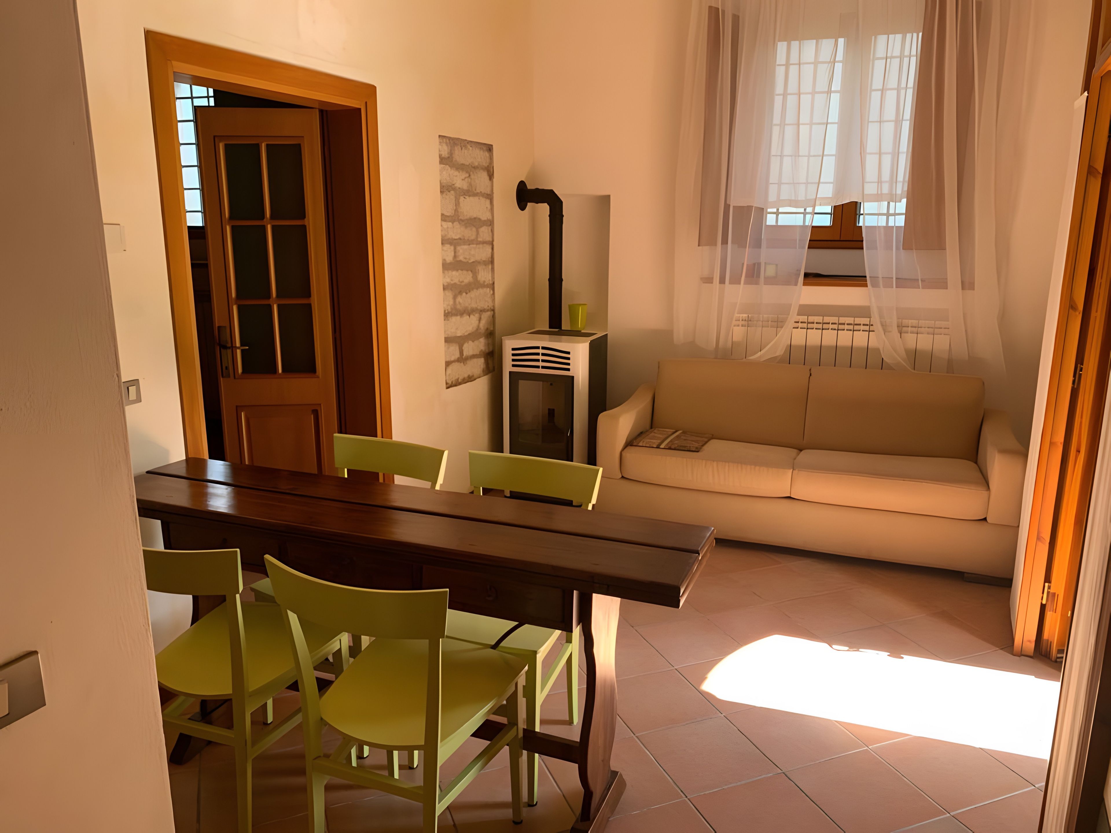 A dining area with a wooden table and chairs, a sofa, and a window with sheer curtains.