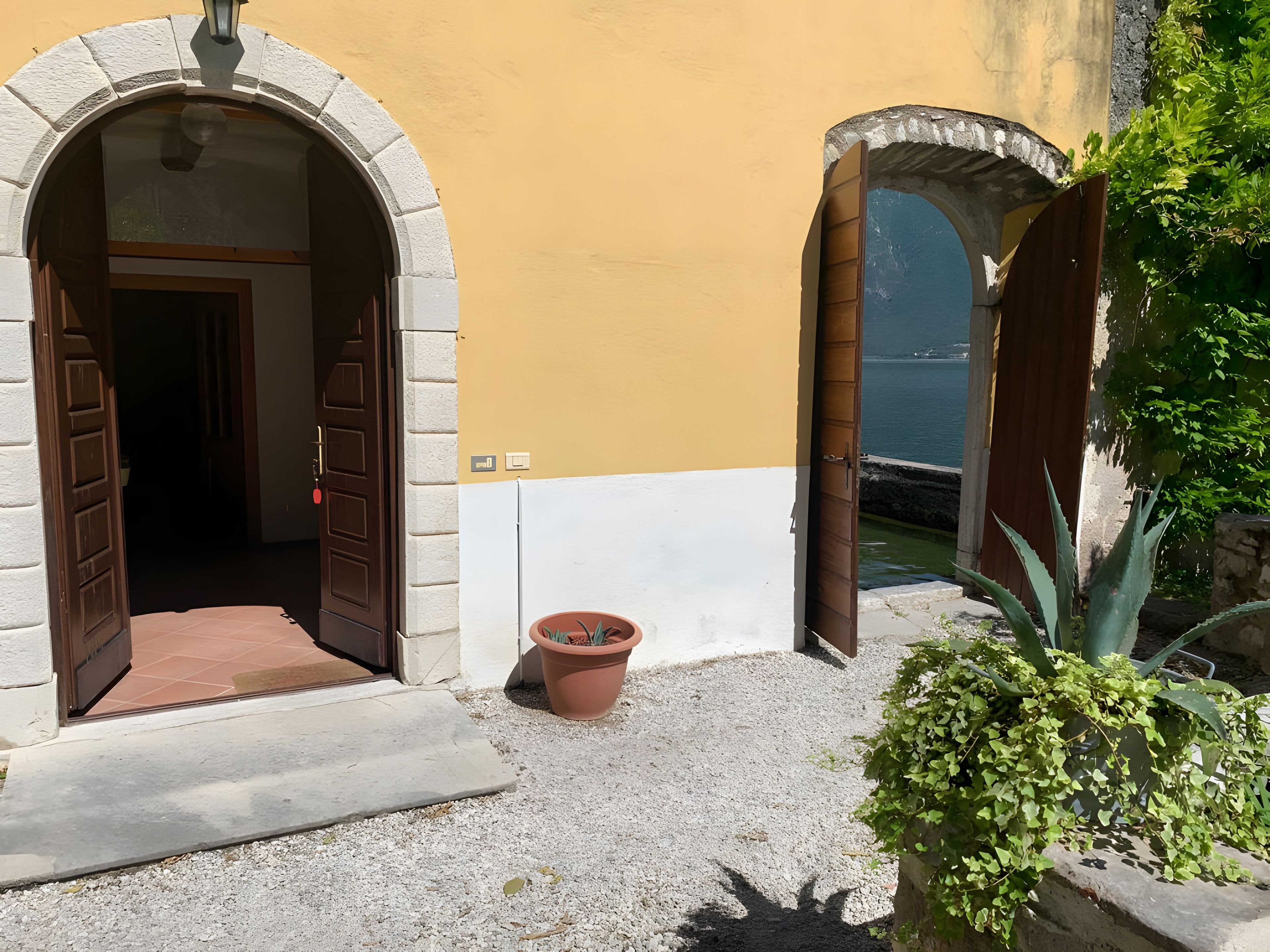 An entrance with two open wooden doors leading to a building, a potted plant, and a view of the sea.