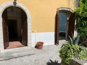An entrance with two open wooden doors leading to a building, a potted plant, and a view of the sea. - Apartment 'Villa Garbera' with Lakeside Dock, Private Garden and Wi-Fi (Limone Sul Garda)