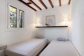 Quarto com duas camas de solteiro, janela, prateleira com uma moldura e duas luminárias de cabeceira.