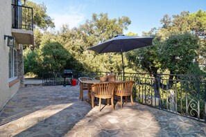 Eine Terrasse im Freien mit Tisch und Stühlen, einem schwarzen Sonnenschirm und einem Steinboden.