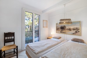 Ein Schlafzimmer mit zwei Betten, einem Sessel, einem Gemälde und einem Fenster mit Blick auf Bäume.