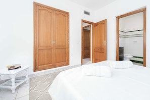 Une chambre d’hôtel avec un grand lit, deux armoires, une petite table avec des livres et une salle de bain équipée d’un miroir et de toilettes.