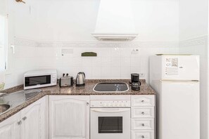 A kitchen with white cabinets, a microwave, a toaster, a kettle, a coffee maker, a sink, and a refrigerator. - Villa Kiwi - Two Bedroom Villa, Sleeps 4 (El Tosalet)
