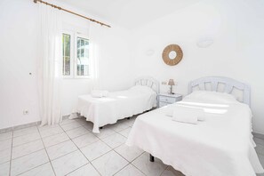 A hotel room with two beds, a window with curtains, a bedside table with a lamp, and a wall-mounted decorative item. - Villa Kiwi - Two Bedroom Villa, Sleeps 4 (El Tosalet)