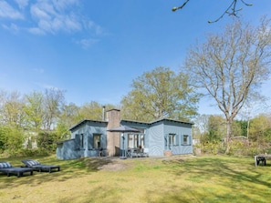 Ein zweistöckiges Haus mit Schornstein, einer Terrasse mit Tisch und Stühlen sowie einem Rasen.