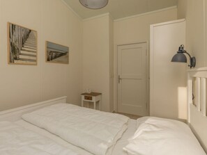 Ein Schlafzimmer mit einem Bett, einem Nachttisch, einer Tür und zwei gerahmten Bildern an der Wand.