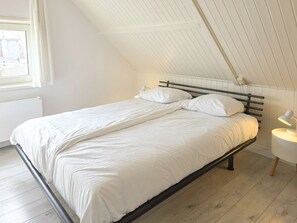 Ein Einzelbett mit Metallgestell und weißer Bettwäsche in einem Zimmer mit schrägen Decken und Holzboden.