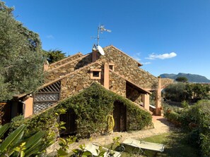A stone house with a sloped roof, a satellite dish, and a garden with plants and a wooden gate. - Holiday Home in Golfo Aranci With Bathtub (Golfo Aranci)