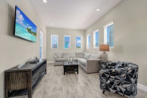 A living room with a flat-screen TV, a sectional sofa, a coffee table, and a patterned armchair. - Lemon Tide Cottage | Private Pool + Margaritaville & Waterpark Access - 2914SR (Kissimmee)