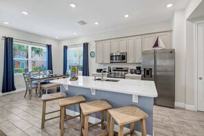 A modern kitchen with a central island, stainless steel appliances, and a view to the outside. - Lemon Tide Cottage | Private Pool + Margaritaville & Waterpark Access - 2914SR (Kissimmee)