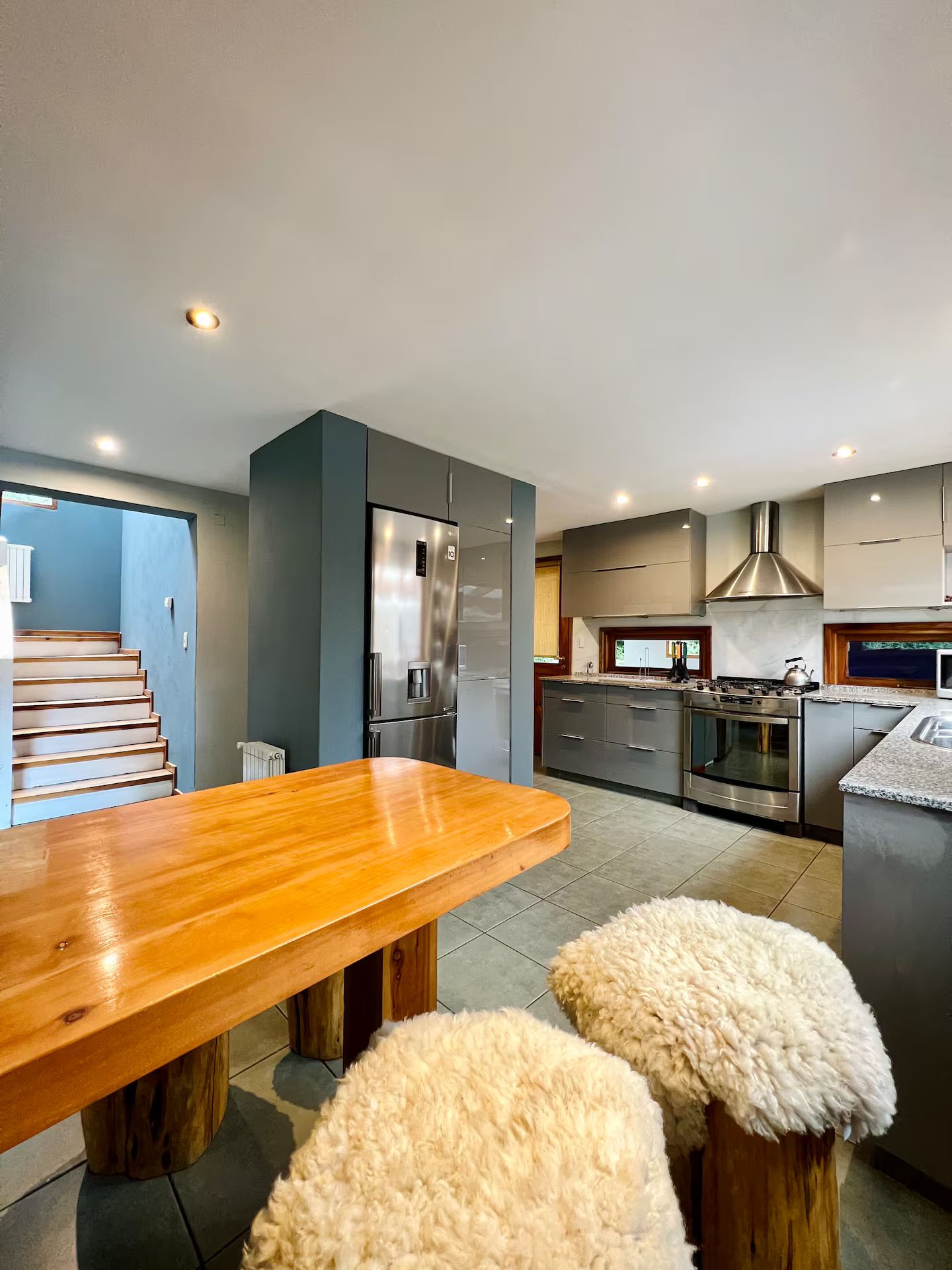 A modern kitchen with a wooden dining table, stainless steel appliances, and a staircase leading to an upper level.