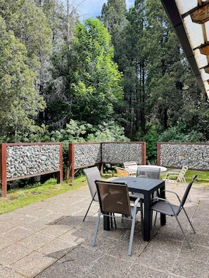 Een terras met een stenen muur, metalen stoelen en een tafel.