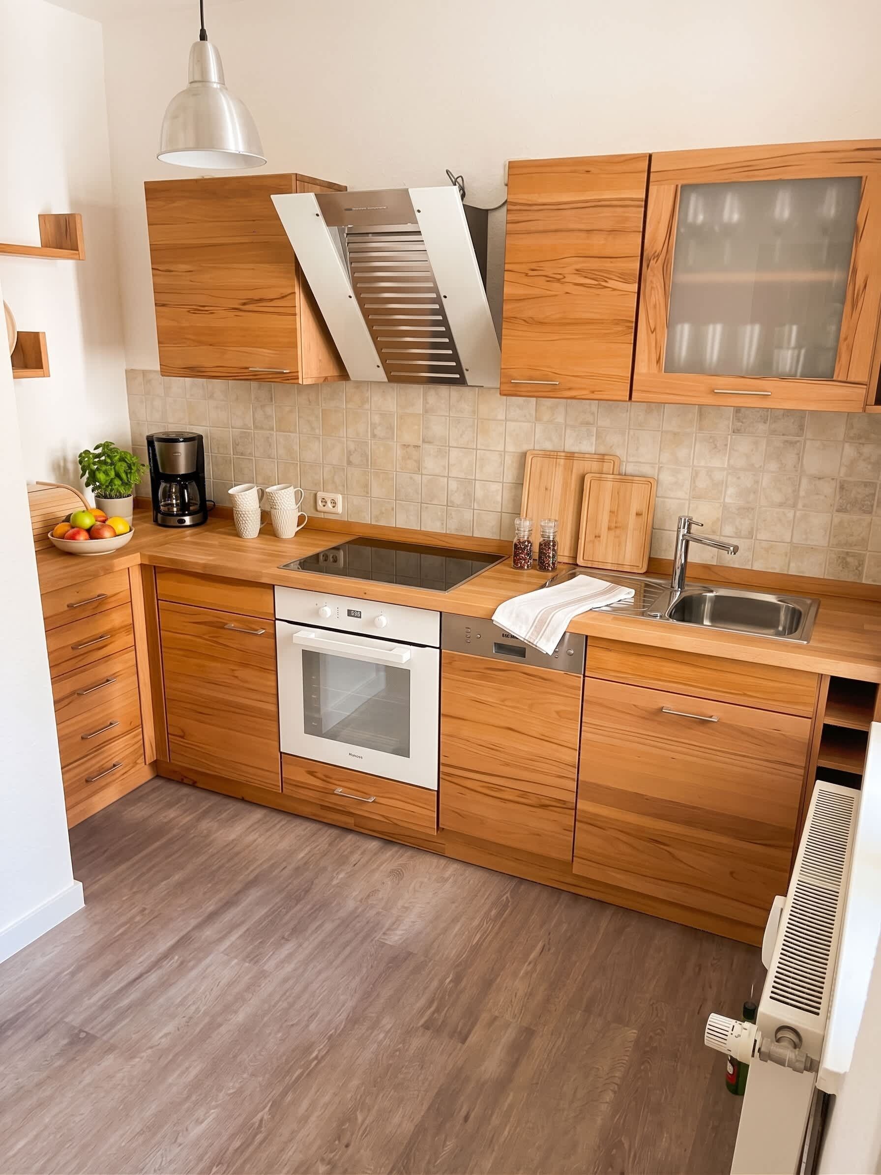 Eine moderne Küche mit Holzschränken, einem eingebauten Backofen, einer Edelstahl-Spüle und einer Pendelleuchte.