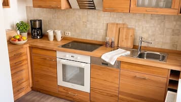 Eine moderne Küche mit Holzschränken, einem eingebauten Backofen, einer Edelstahl-Spüle und einer Pendelleuchte.