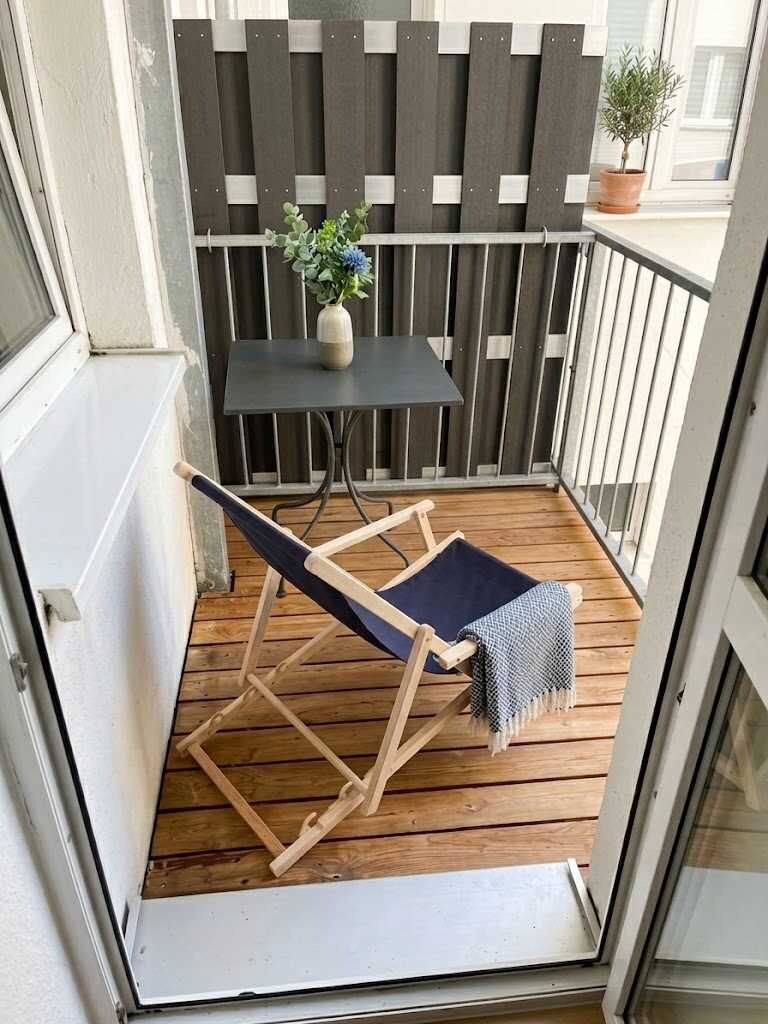 Ein Balkon mit Holzboden, einem Klappstuhl, einem kleinen Tisch und einem Topfpflanzen.