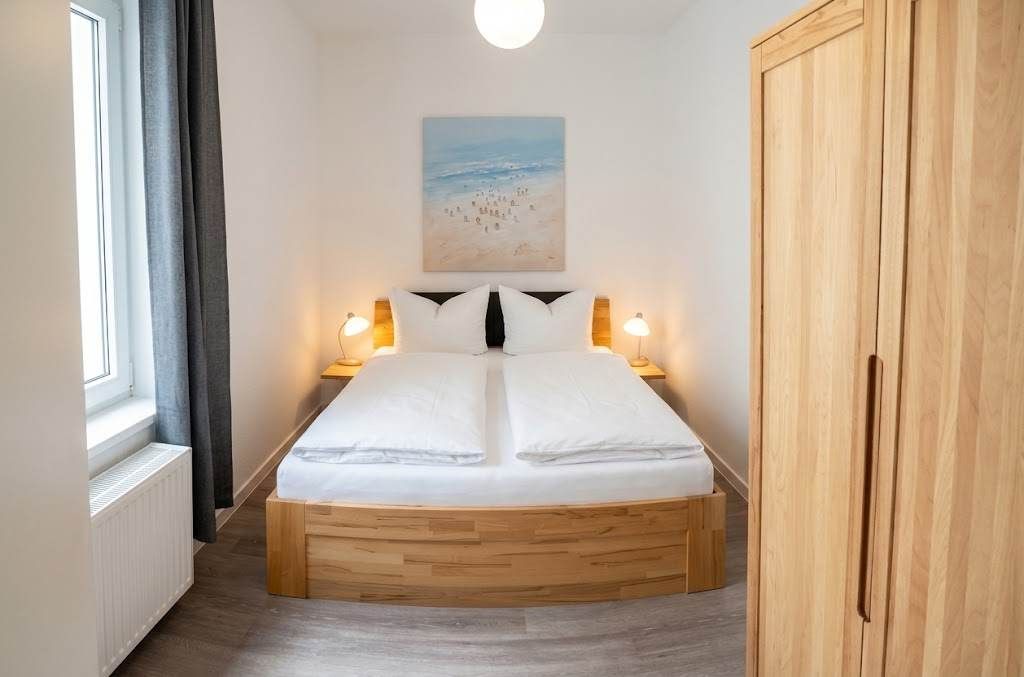 A bedroom with a bed, bedside lamps, a painting on the wall, and a wardrobe.