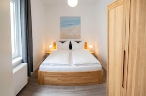A bedroom with a bed, bedside lamps, a painting on the wall, and a wardrobe. - Gemütliche Wohnung Leonhardstraße (Rostock)