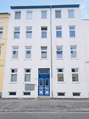 En bygning med flere etager, en blå dør i midten, mange vinduer og en synlig garageport.