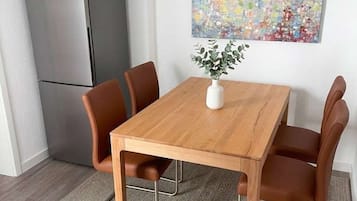 Ein Essbereich mit einem Holztisch und vier Stühlen, einer kleinen weißen Vase mit einer Pflanze sowie einem farbenfrohen, abstrakten Gemälde an der Wand.