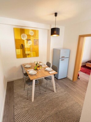 A dining area with a wooden table set for two, a small refrigerator, and a wall-mounted light fixture. - Ruhige Wohnung Leonhardtstraße (Rostock)