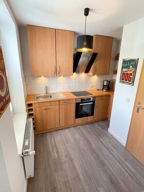 A compact kitchen with wooden cabinets, a sink, a stove, and a hanging light fixture. - Ruhige Wohnung Leonhardtstraße (Rostock)