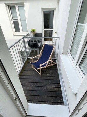 A balcony with a wooden chair and a small table, a potted plant, and a window with blinds. - Ruhige Wohnung Leonhardtstraße (Rostock)