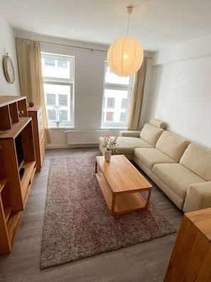 A modern living room with a sofa, a wooden coffee table, a rug, and a hanging light fixture. - Ruhige Wohnung Leonhardtstraße (Rostock)
